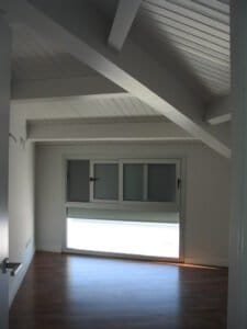 Interior de golfes amb sostre de fusta blanca i gran finestra