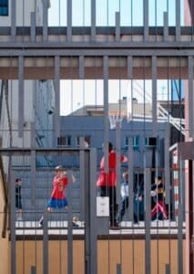 Escola del Carme: pati interior amb reixa metàl·lica i nens jugant bàsquet