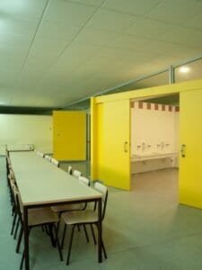 Interior rehabilitat Escola del Carme, Sabadell: menjador, lavabos i portes corredisses grogues.