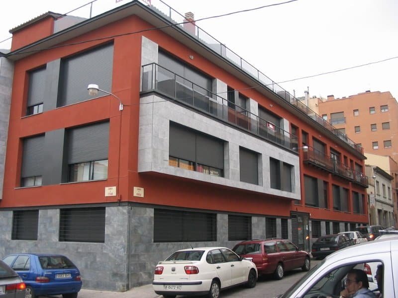 Vista en cantonada d’un edifici residencial a Sabadell amb balcons, façana ceràmica i sòcol de pedra
