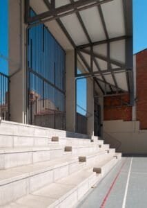 Detall constructiu: grades de formigó i coberta metàl·lica en pati escolar.