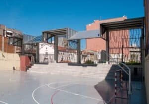 Pati amb pista esportiva, grades i cobertes metàl·liques al projecte Carmelites.